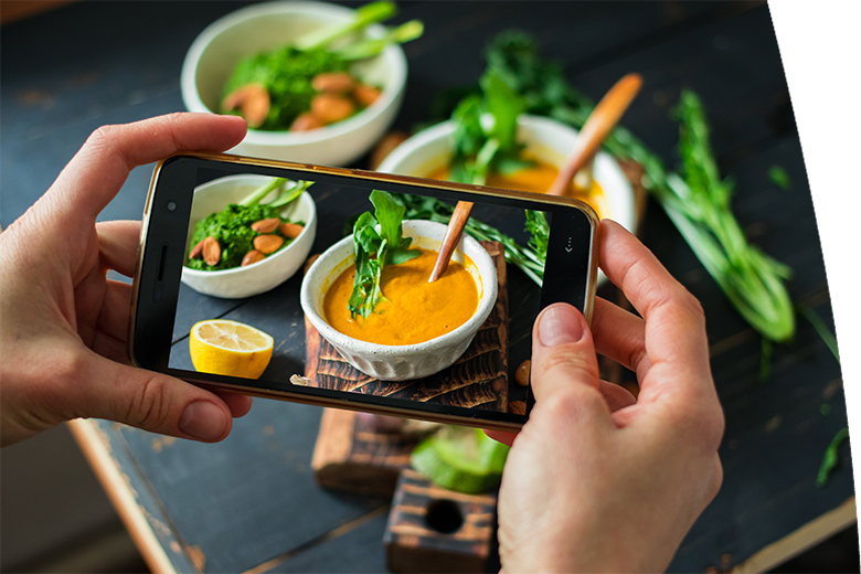 Woman hands makes phone food photo of lunch or dinner with creamy pumpkin soup dip squash on wooden board with vegetables.